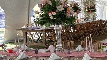 One of the farm's wooden farm tables dressed for a wedding dinner inside the tent — tabletop, runner, and place settings
