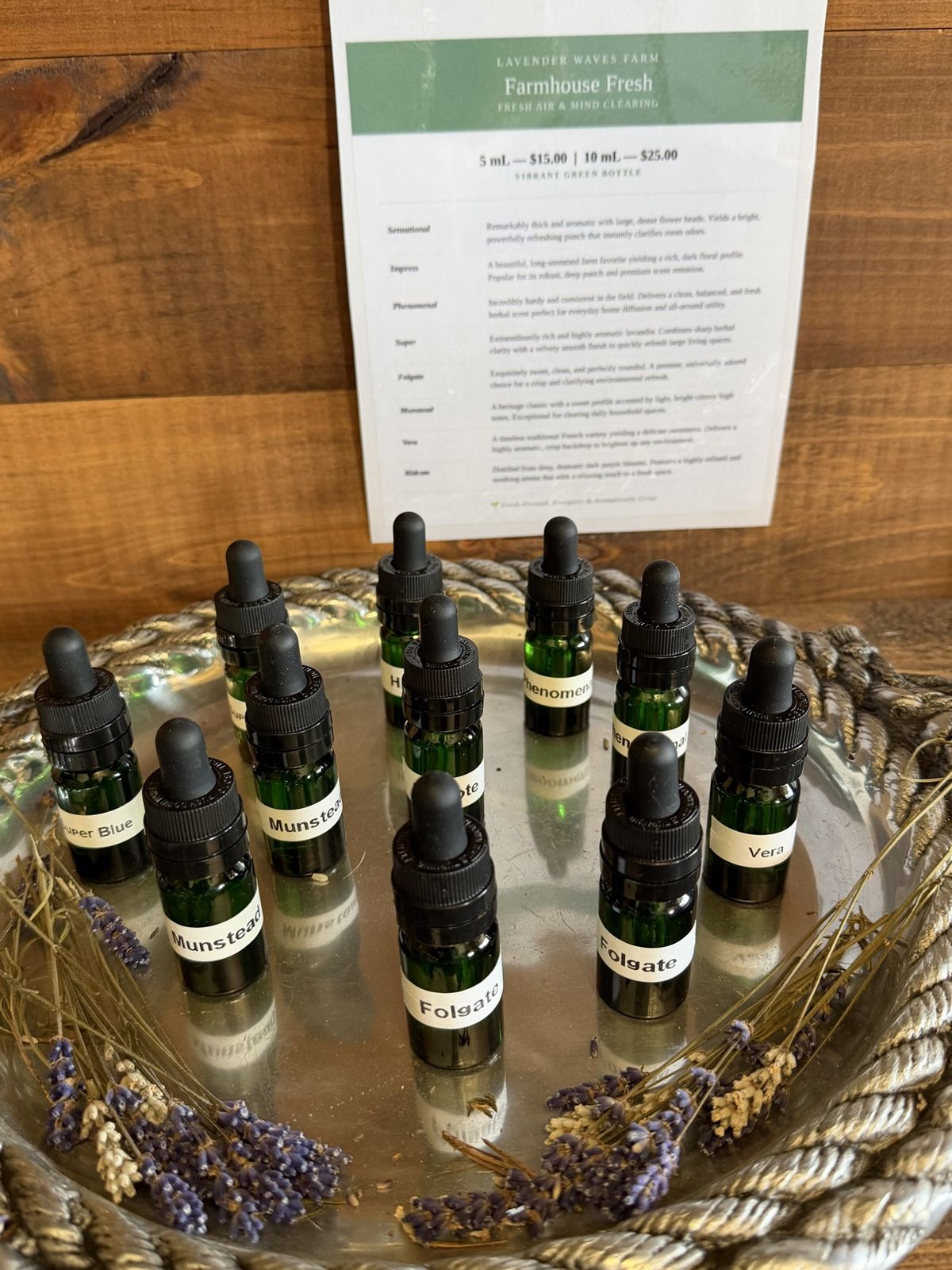 Bottles of the farm's lavender essential oil — green dropper bottles labeled by variety, including Munstead, Folgate, and Super Blue — on a tray with dried lavender