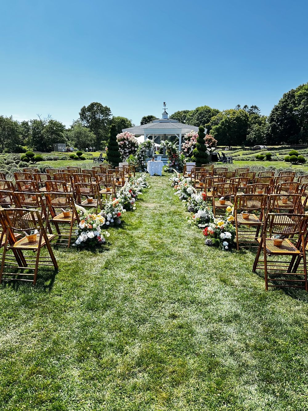 A wedding aisle lined with flowers leading to the gazebo, with the farm's bamboo chairs